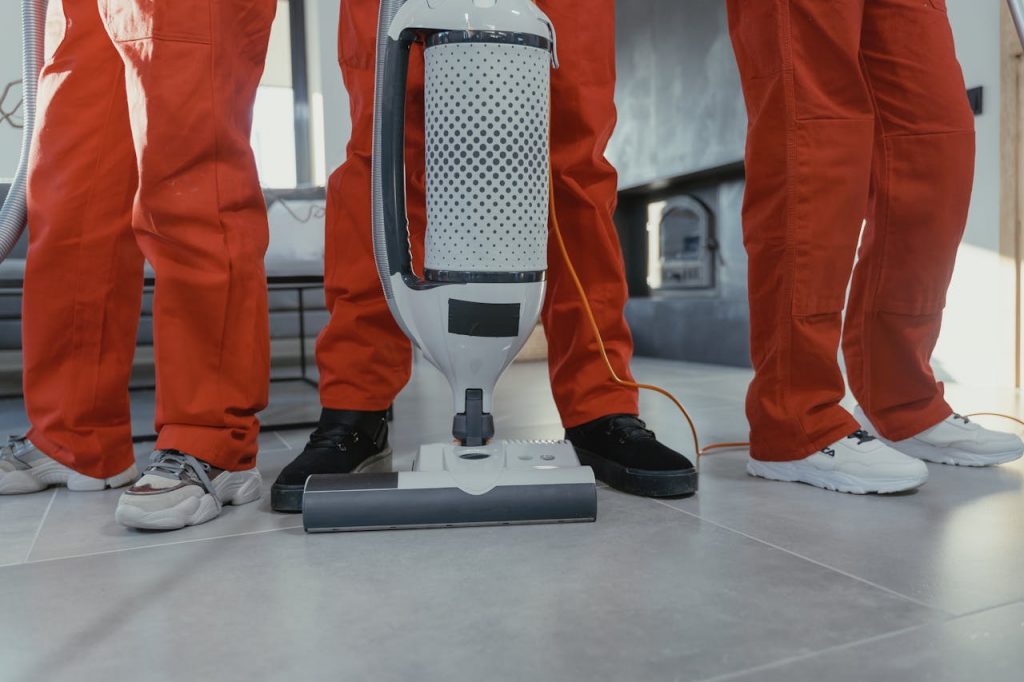 pexels-photo-6195122 Team of professional cleaners in red uniforms using a vacuum cleaner indoors.